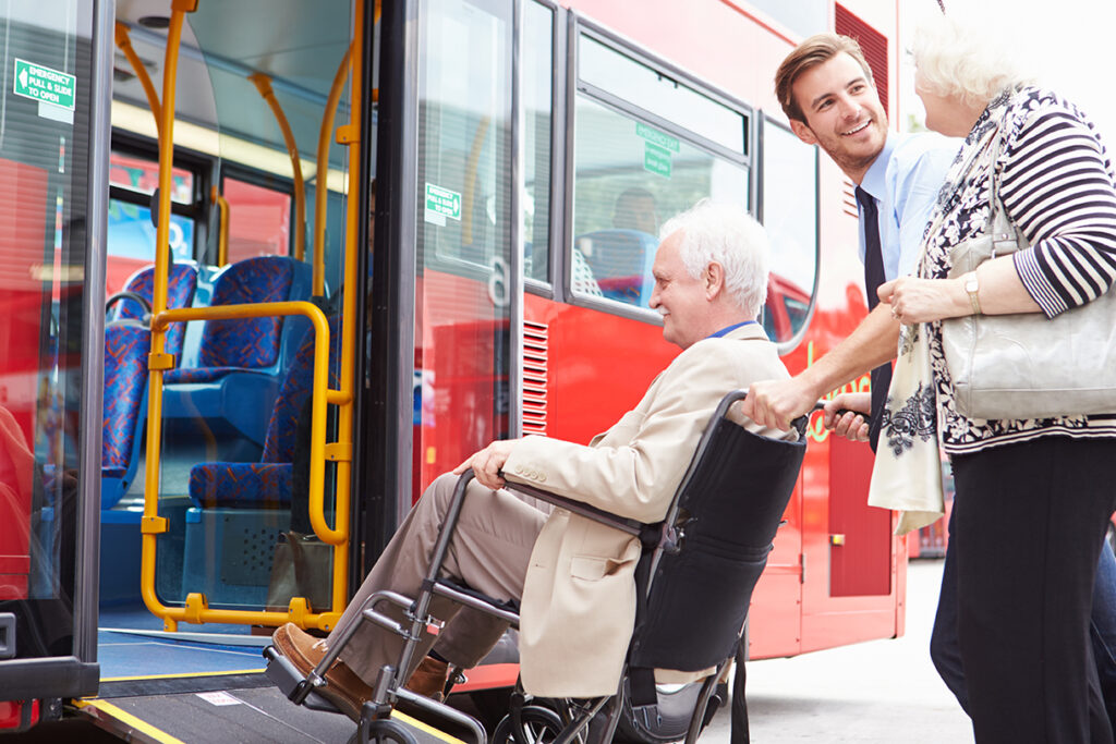 Driver helping senior couple board bus via wheelchair ramp